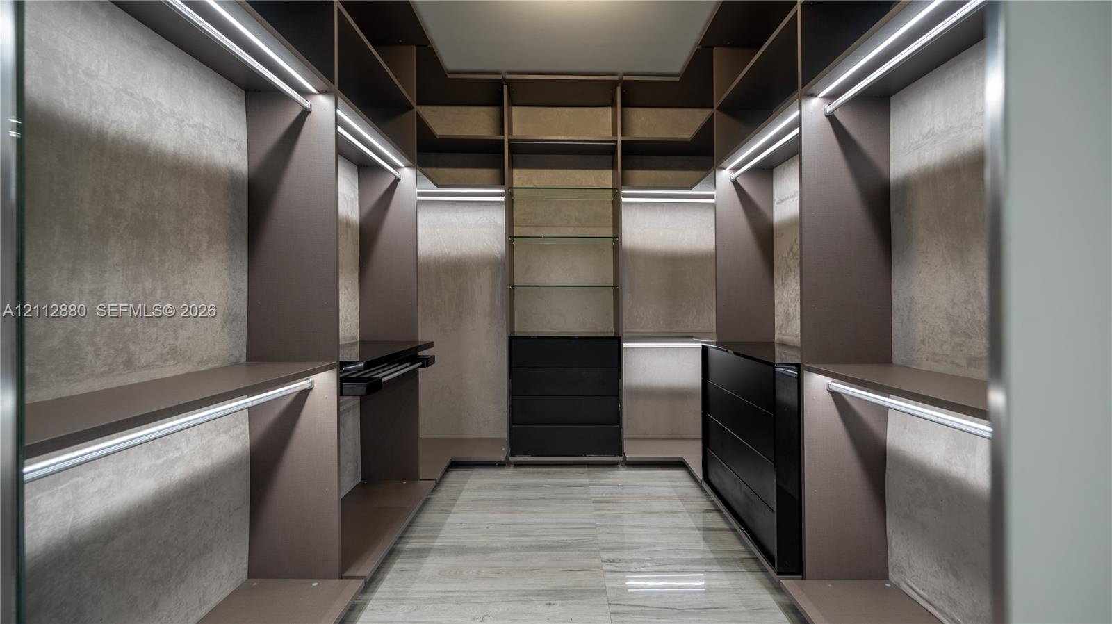 Custom walk-in closet featuring extensive built-in cabinetry, integrated LED strip lighting, open shelving, a multi-drawer dresser unit