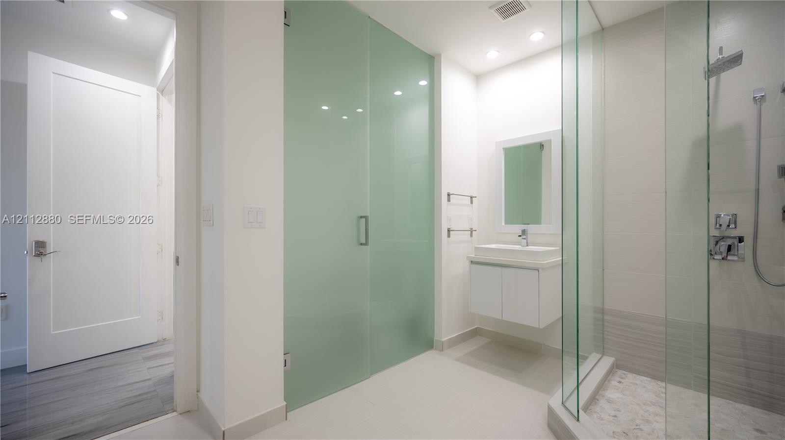 Bathroom featuring a floating vanity with a vessel sink, a walk-in shower with a glass enclosure, a rainfall showerhead, and a frosted-glass door
