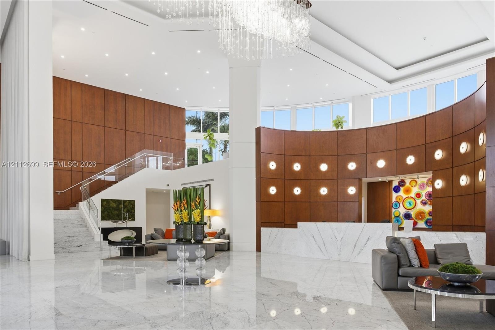 Grand foyer featuring floor-to-ceiling wood paneling, curved architectural walls, polished stone flooring, a multi-tiered crystal chandelier, and a st