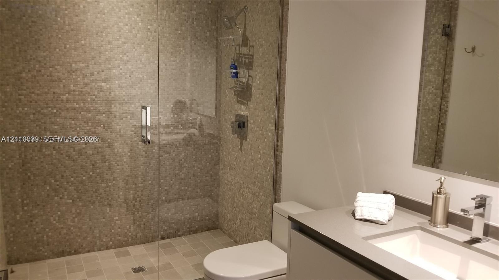Walk-in shower featuring a glass enclosure and tiled surround, flat-panel vanity with a solid-surface countertop, rectangular undermount sink, and wal