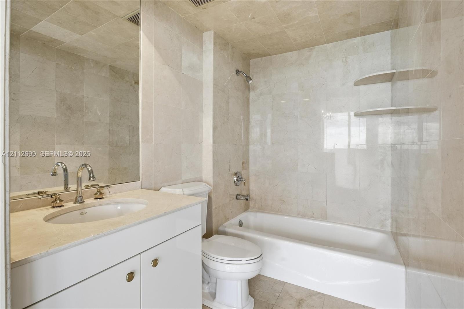 Full-height stone tile wall treatments, integrated floating stone shelving, undermount sink with polished chrome hardware, custom white cabinetry with