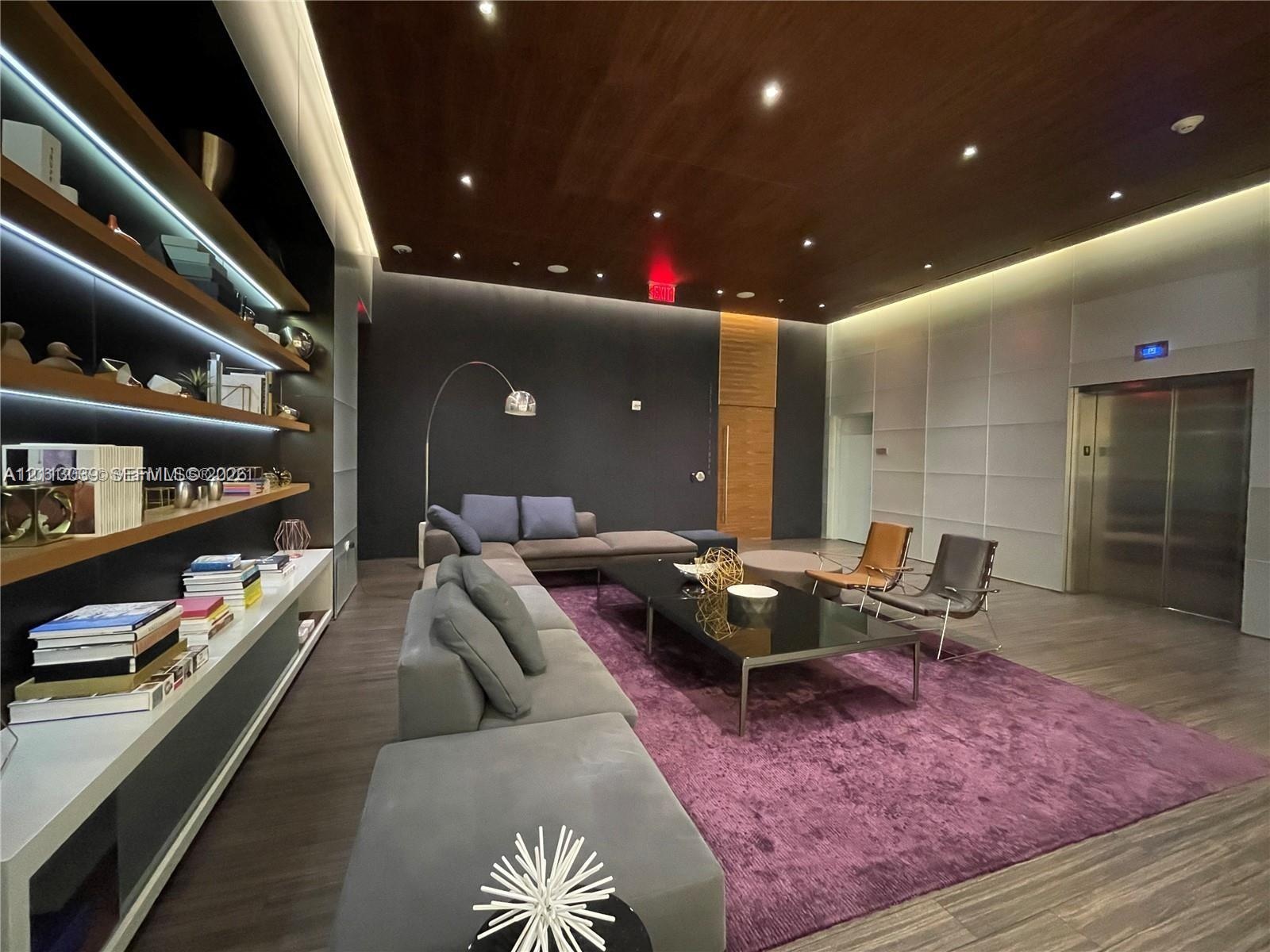 Wood-finish ceiling panels, recessed lighting, built-in shelving with integrated LED illumination, metallic elevator doors, and wood-finish flooring
