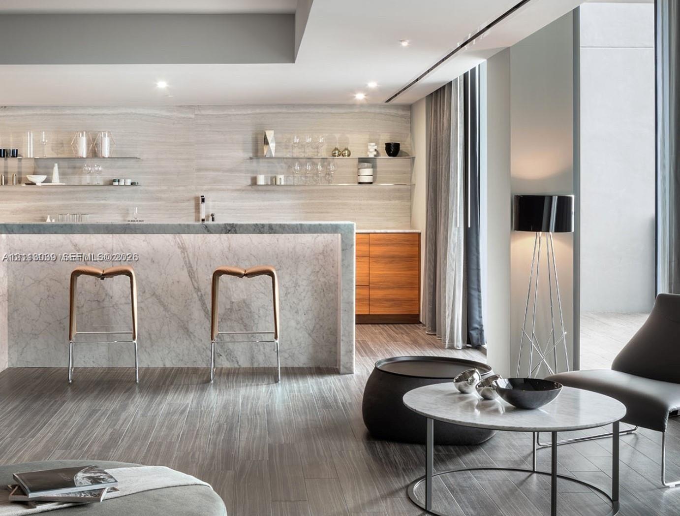 Stone-surfaced kitchen island with waterfall edge, wood-finish flooring, custom wood-tone cabinetry, and tiered glass shelving