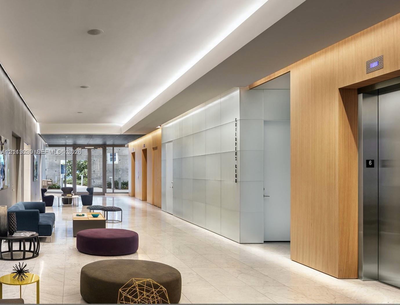 Modern lobby featuring large-format stone flooring, wood-panel wall accents, recessed cove lighting, and floor-to-ceiling frosted glass paneling