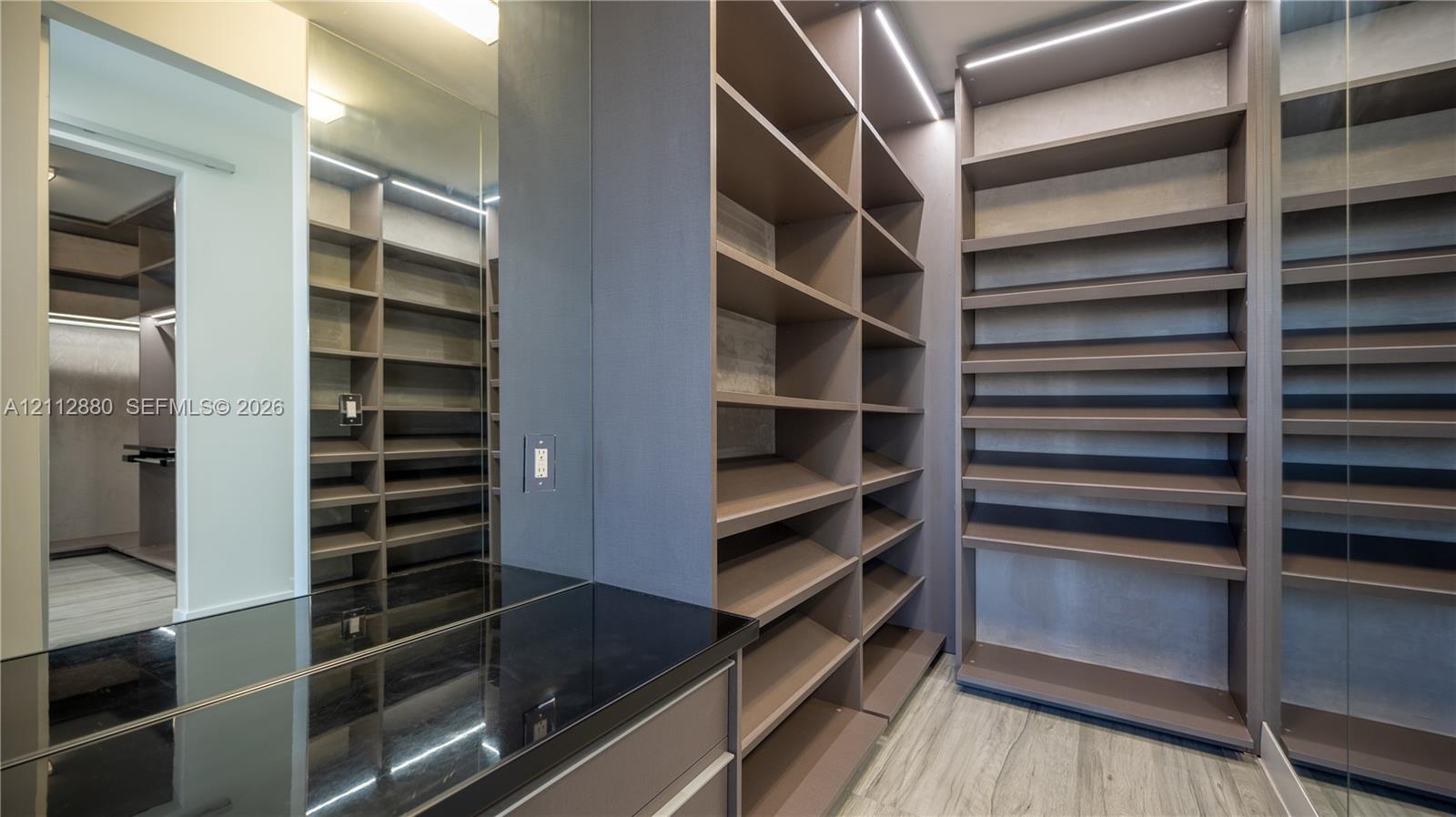 Custom walk-in closet featuring extensive built-in shelving, integrated strip lighting, full-length mirror panels, a dark-toned countertop,