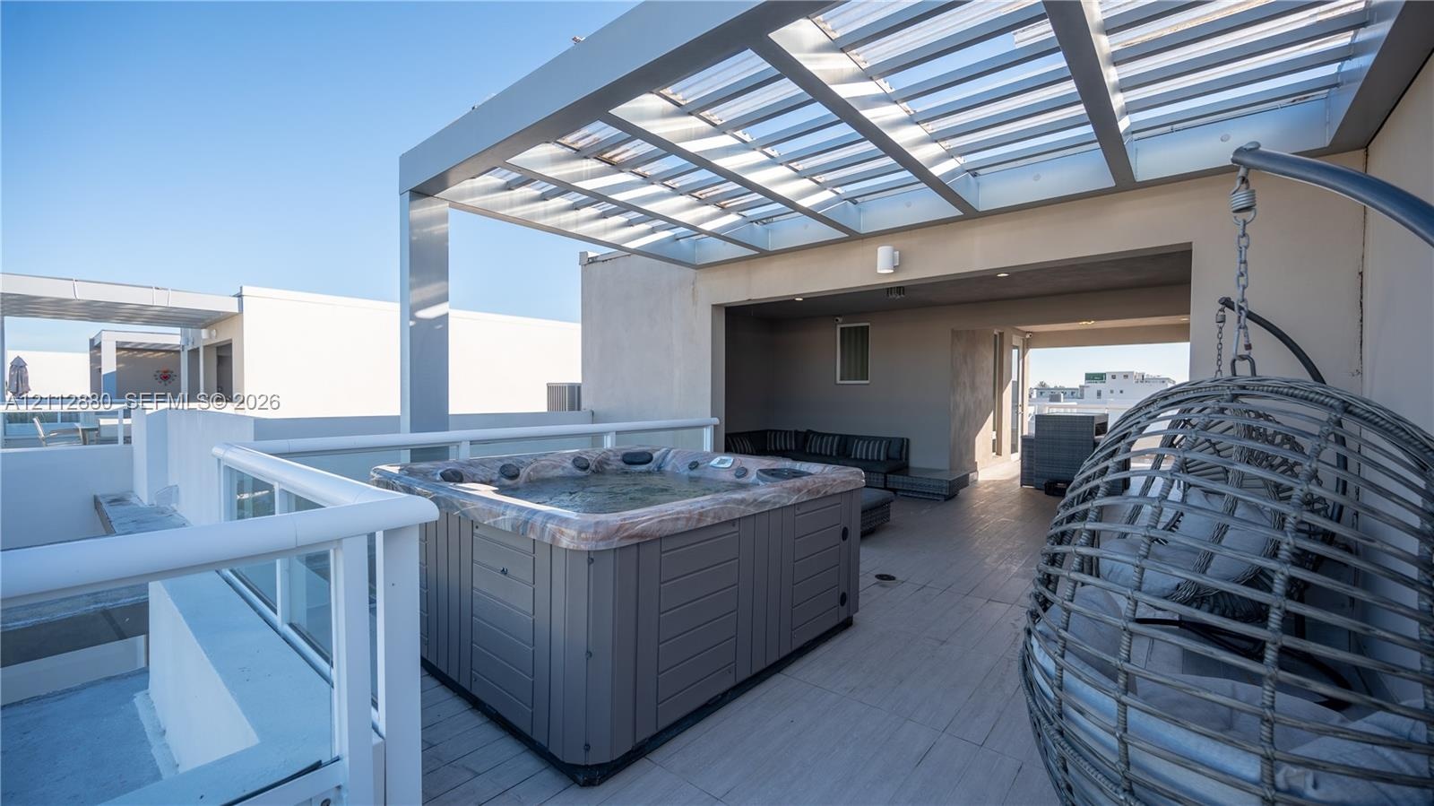 Rooftop terrace featuring a built-in hot tub, slatted metal pergola, tile flooring, and white glass-panel railings