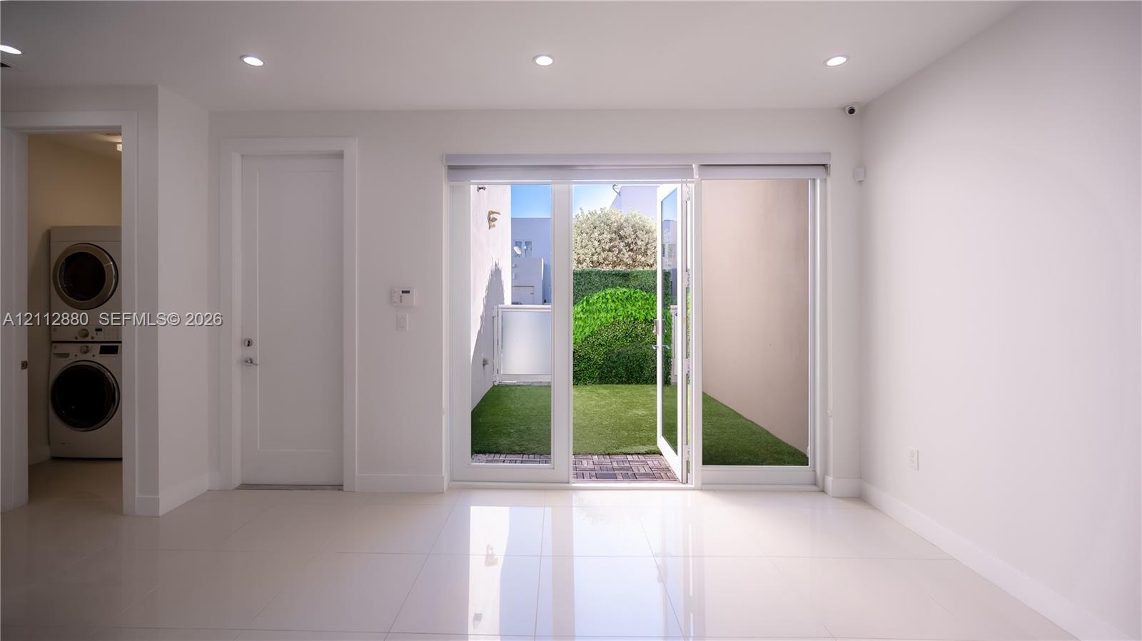 Bright interior space featuring polished tile flooring, recessed lighting, and a glass-paneled door opening to a private patio area with artificial tu