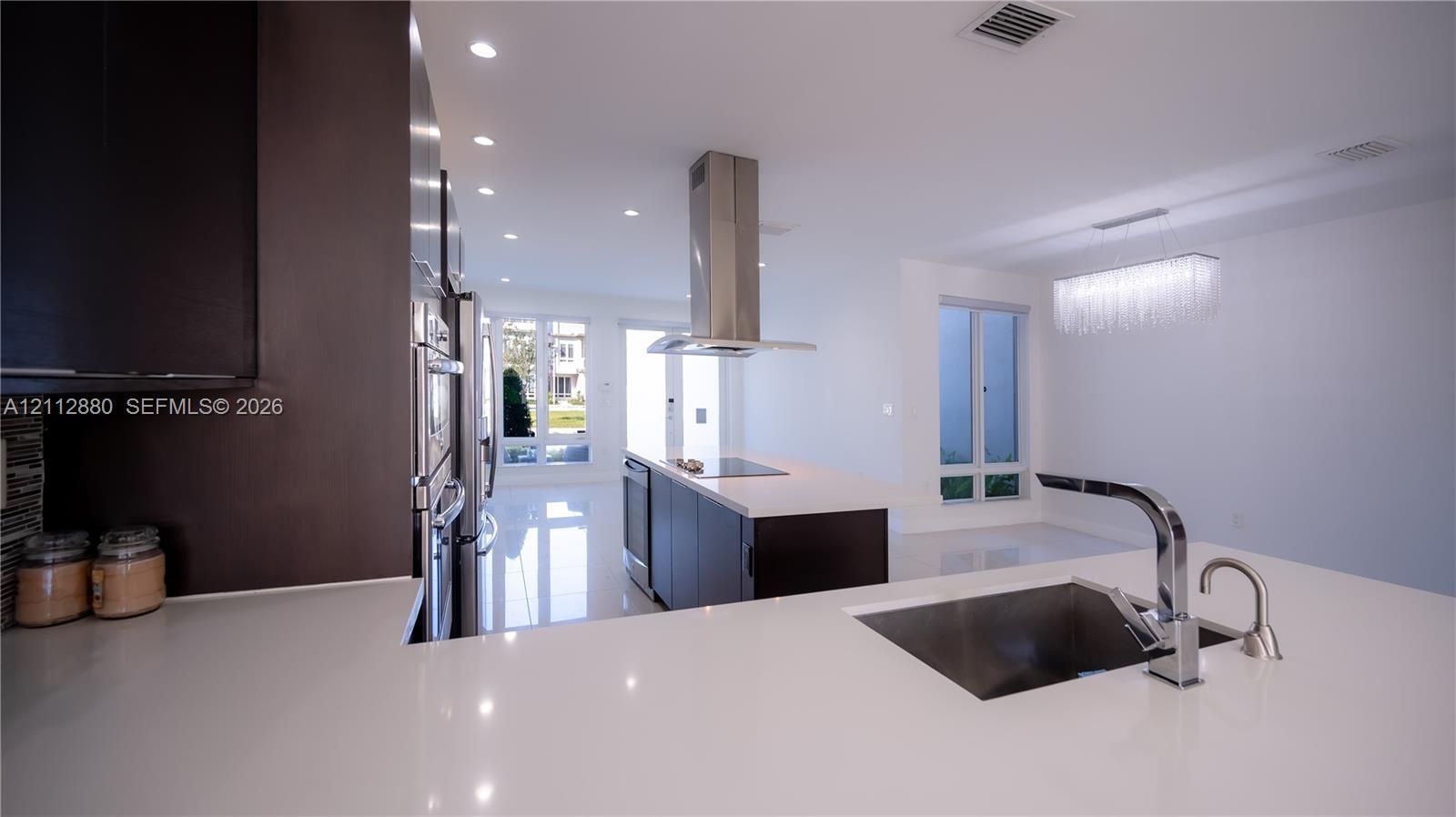Kitchen featuring a center island with a stainless steel range hood, stone-surface countertops, custom flat-panel cabinetry, and integrated stainless 