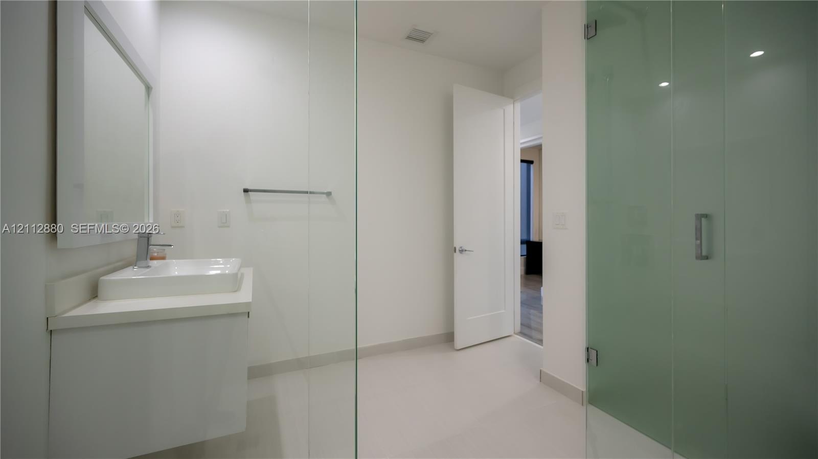 Bathroom featuring a floating vanity with a rectangular vessel sink, wall-mounted mirror, walk-in shower with glass enclosure, and tile flooring