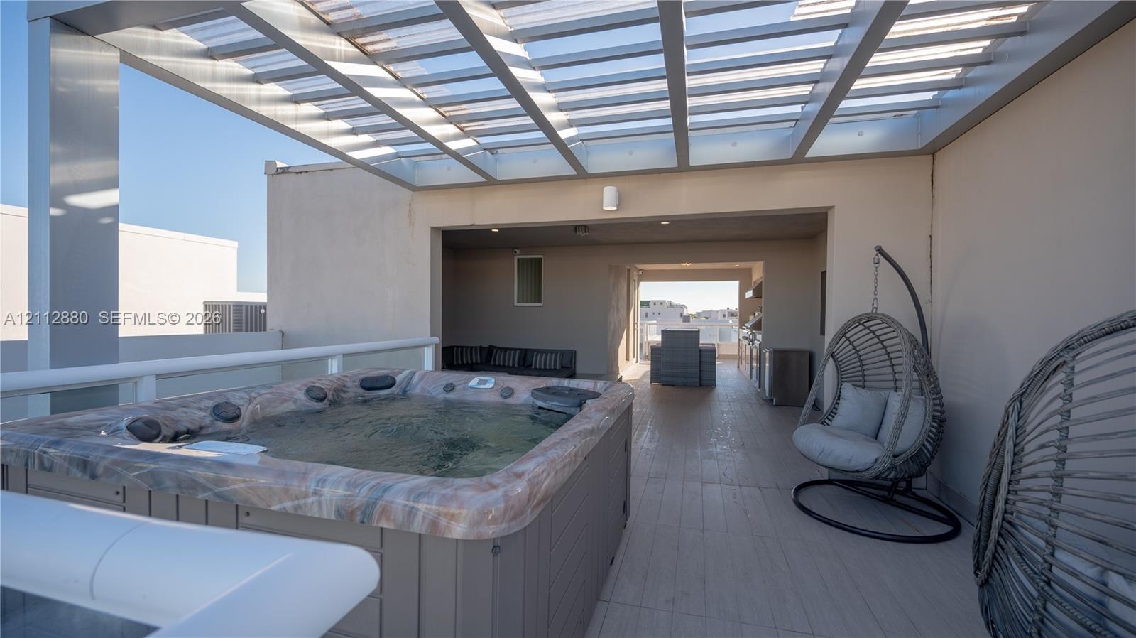 Rooftop terrace featuring a built-in spa, metal-frame pergola, wood-finish decking, and an integrated outdoor kitchen area