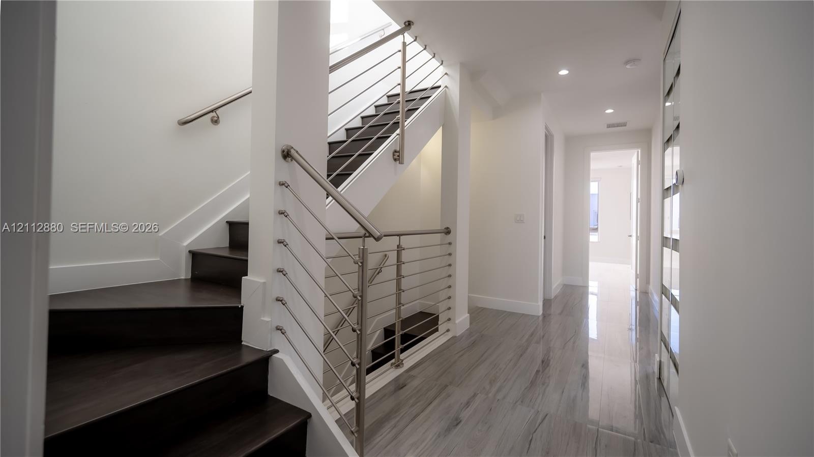 Staircase featuring dark wood-finish treads, a metal tension-cable railing, and a minimalist handrail, complemented by large-format tile flooring and 