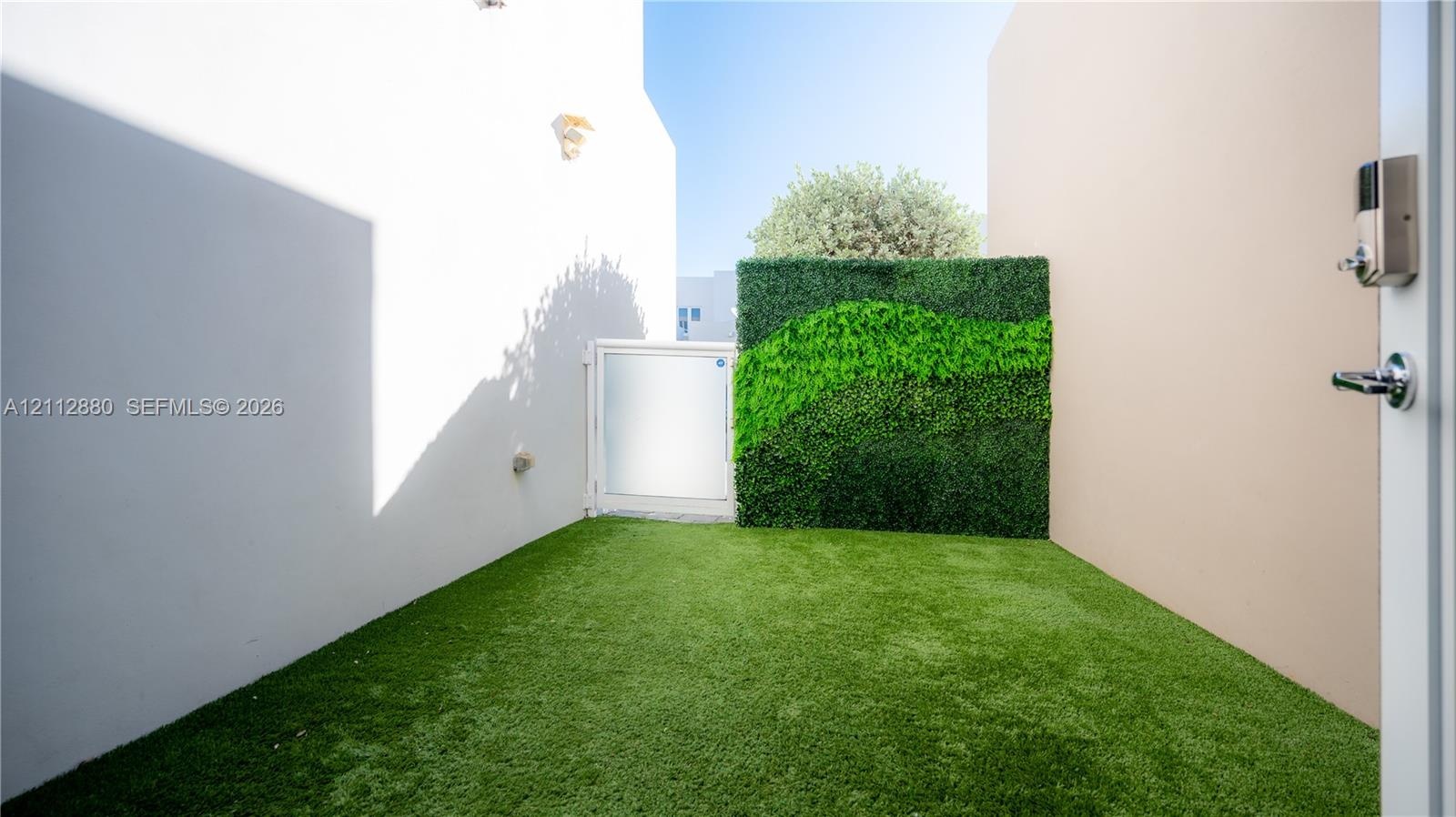 Exterior patio featuring artificial turf, a decorative vertical green wall, and a white gate