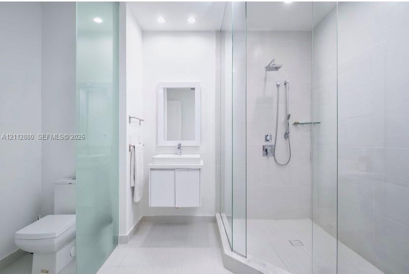 Bathroom featuring a glass-enclosed shower with a rainfall showerhead and handheld sprayer, a floating vanity with a rectangular sink, a recessed wall