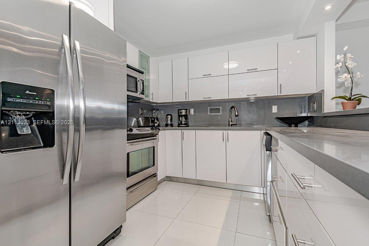 Kitchen featuring high-gloss white cabinetry, stainless steel appliances, solid-surface countertops, a gooseneck faucet, and white tile flooring