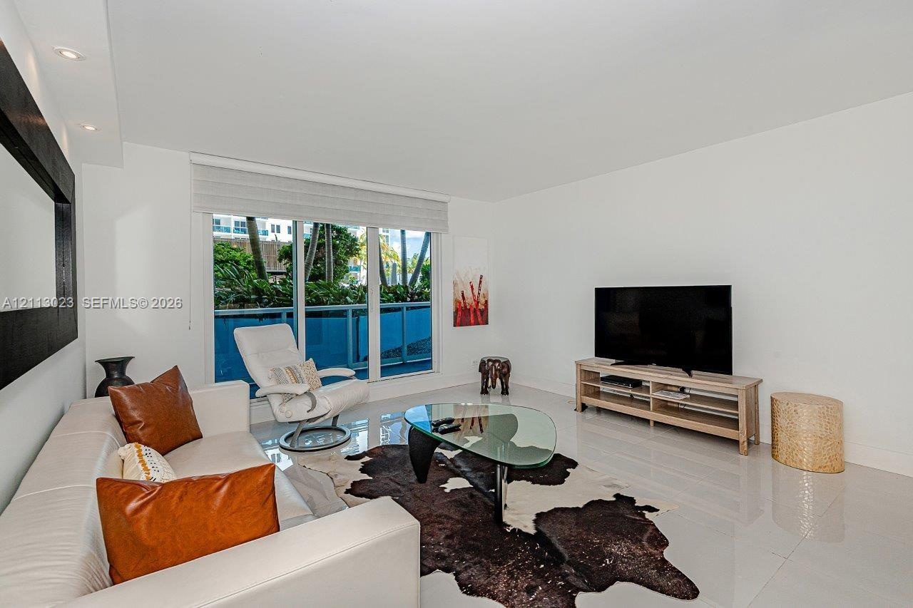Living area featuring neutral tile flooring, recessed ceiling lighting, a built-in recessed wall feature, and floor-to-ceiling windows with a balcony