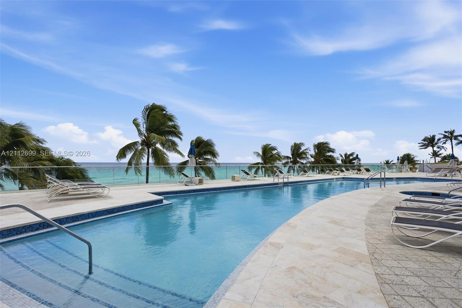Swimming pool with tiered entry steps, stone paver decking, and a glass panel perimeter railing