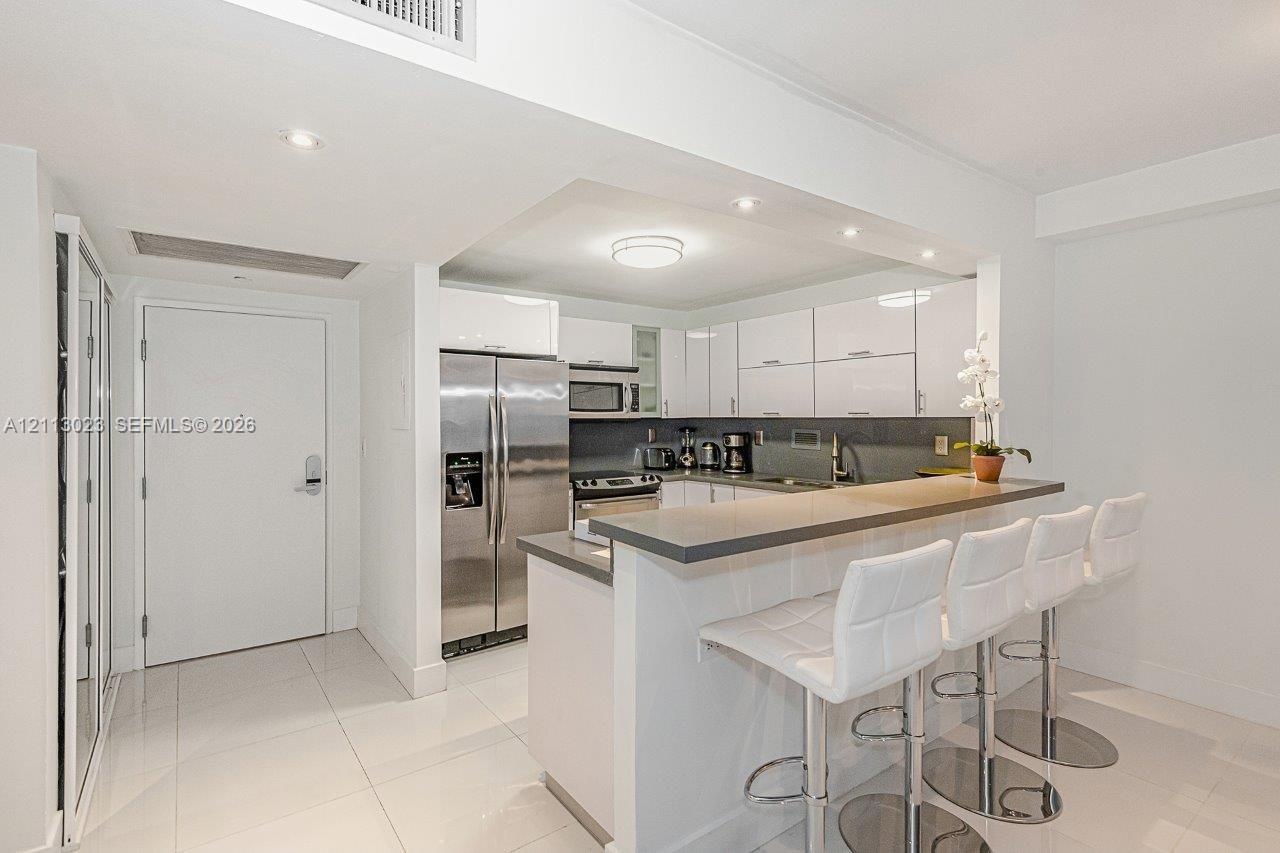 Kitchen featuring white flat-panel cabinetry, stainless steel appliances, a stone countertop peninsula, and polished tile flooring