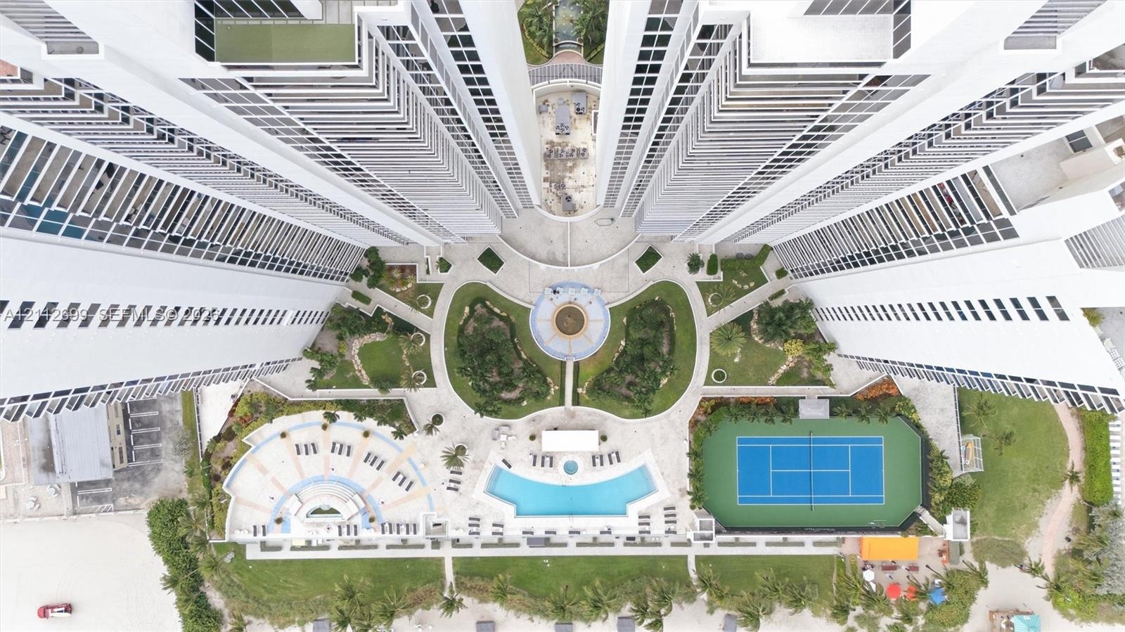 Aerial perspective of high-rise condominium complex featuring a central courtyard with structured landscaping, a swimming pool, a tennis court, and pa