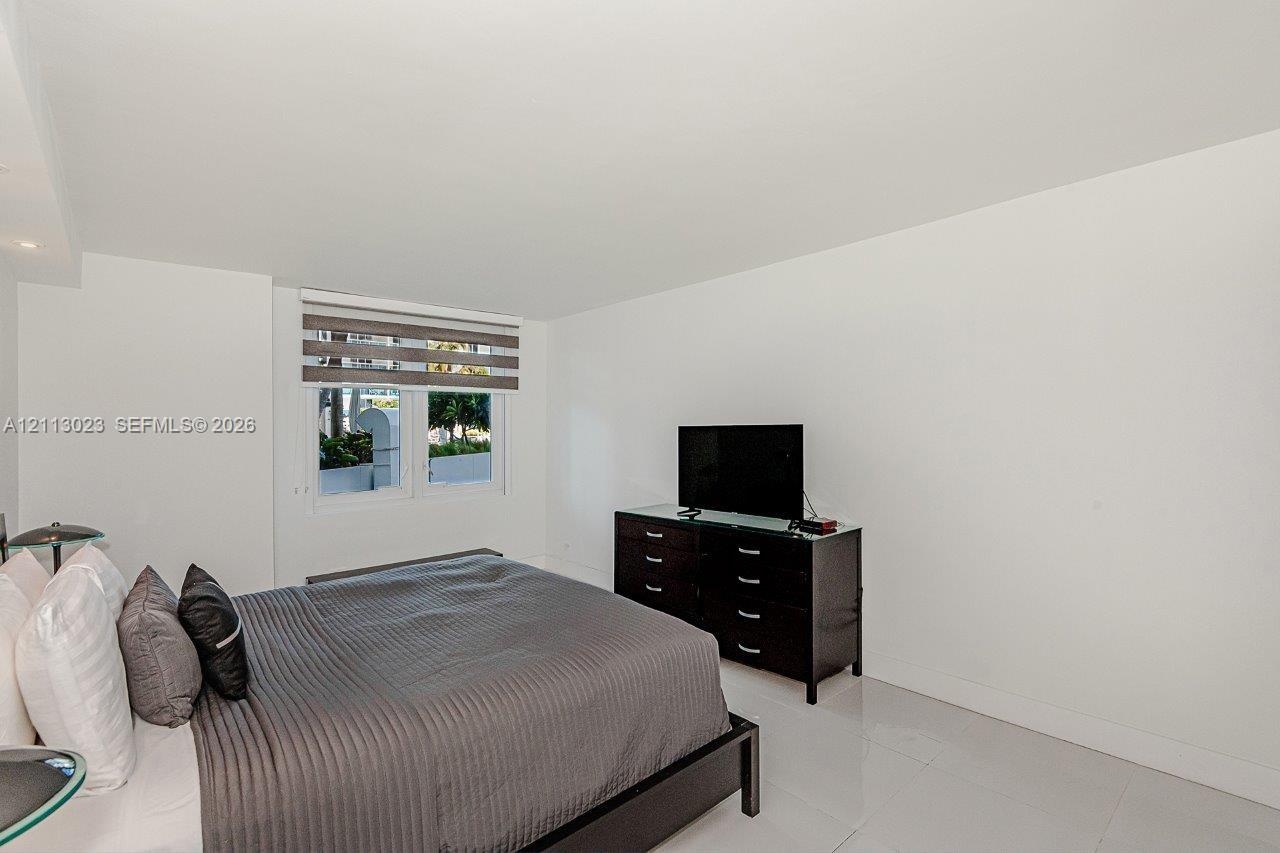 Neutral-toned interior space featuring glossy tile flooring, smooth wall finishes, and a single window with integrated horizontal blinds
