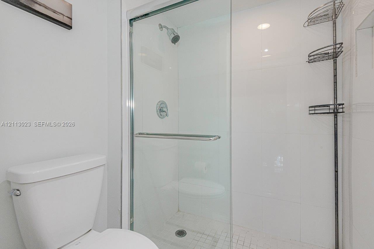 Glass-enclosed shower with white wall tile, mosaic tile shower floor, and chrome fixtures