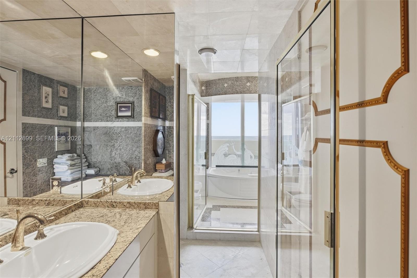 Bathroom featuring a stone-topped dual vanity with integrated sinks, floor-to-ceiling mirrors, tile wall detailing, a jetted soaking tub, and custom p