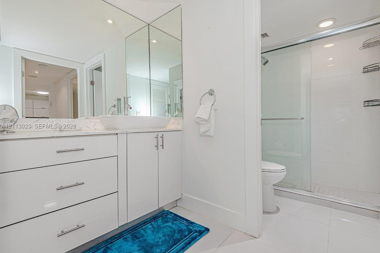 Bathroom featuring a glossy white vanity with a rectangular vessel sink, quartz countertop, full-height wall mirror, and a glass-enclosed shower with 