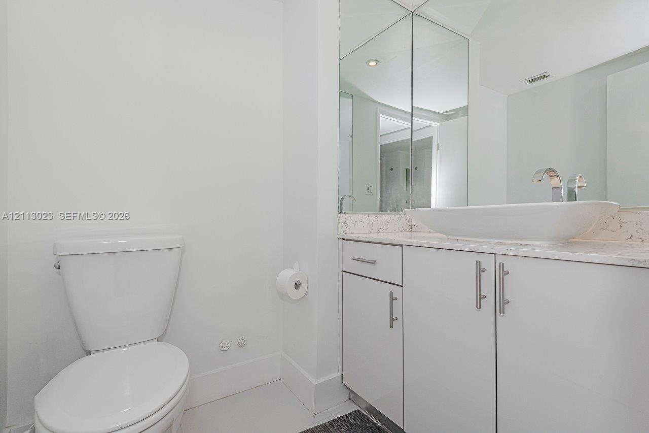 Bathroom featuring a vanity with high-gloss white cabinetry, a stone-composite countertop, a rectangular vessel sink, and a polished chrome faucet, co