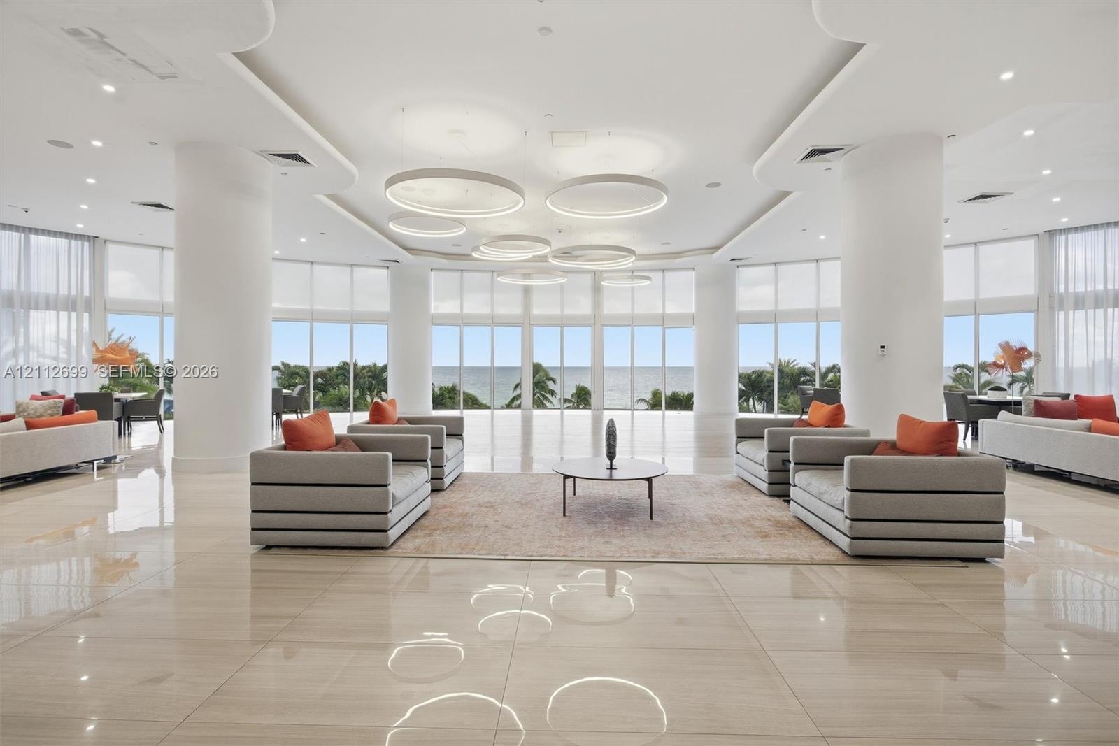 Expansive open-concept space featuring polished stone flooring, floor-to-ceiling windows, sculptural circular pendant lighting, recessed tray ceiling 