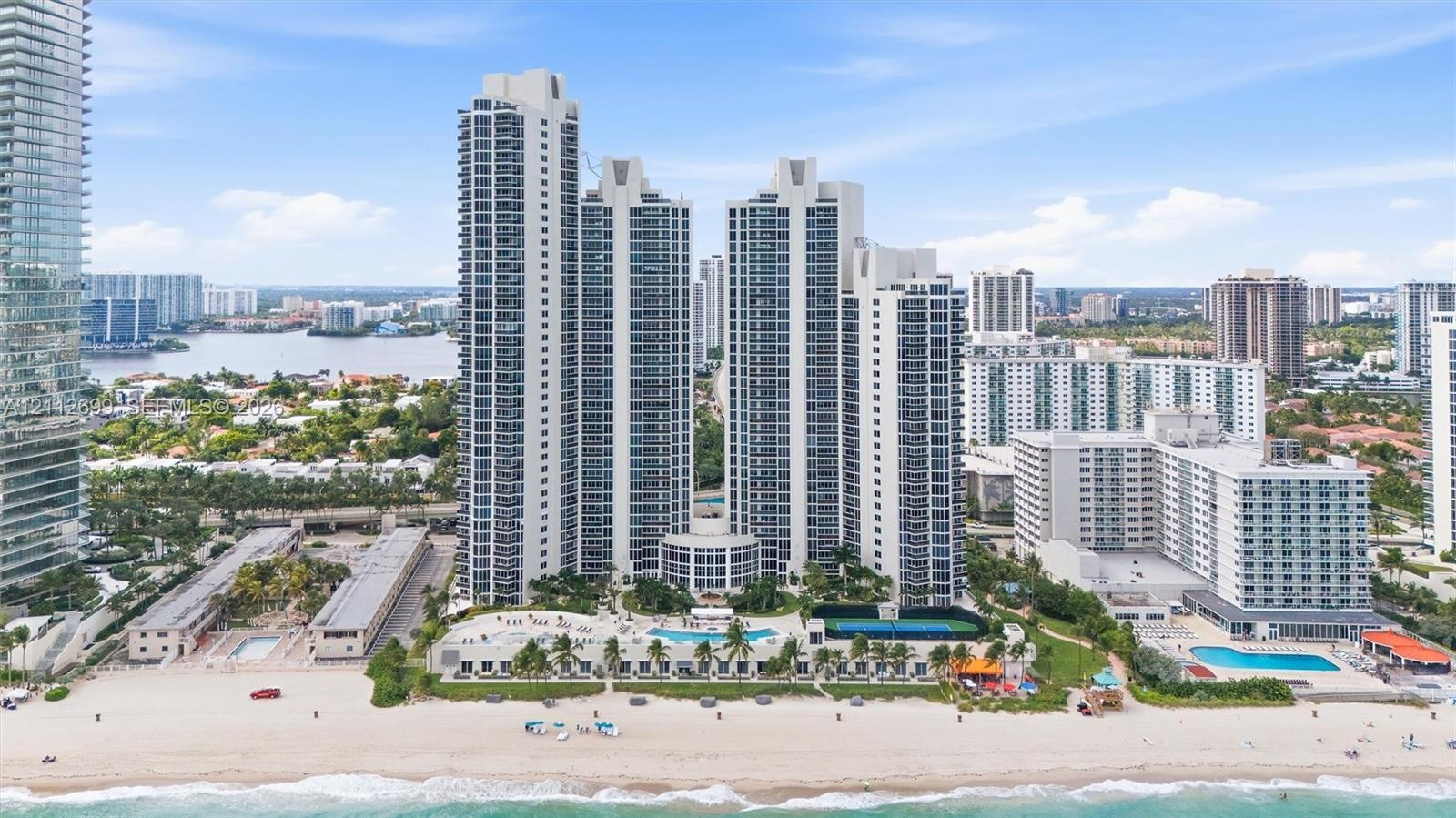 High-rise residential towers featuring direct beach access, an outdoor swimming pool, tennis courts, and landscaped grounds