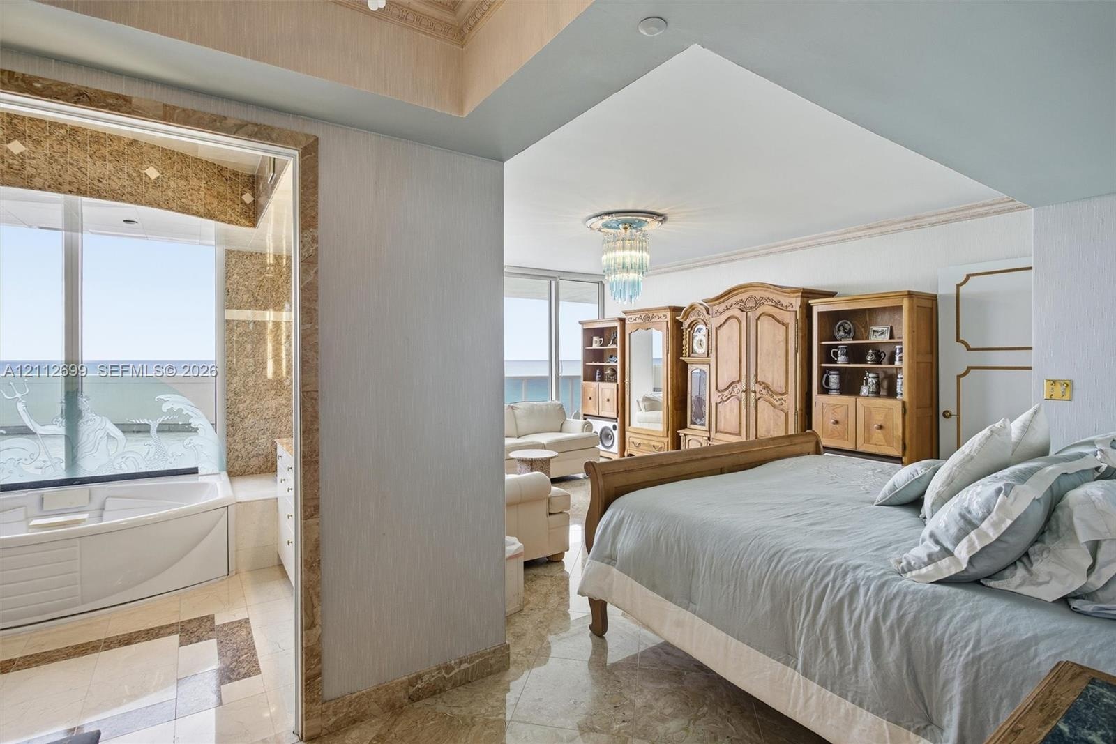 Polished stone flooring, crown molding, built-in recessed lighting, decorative crystal-style chandelier, and jetted corner soaking tub featuring stone