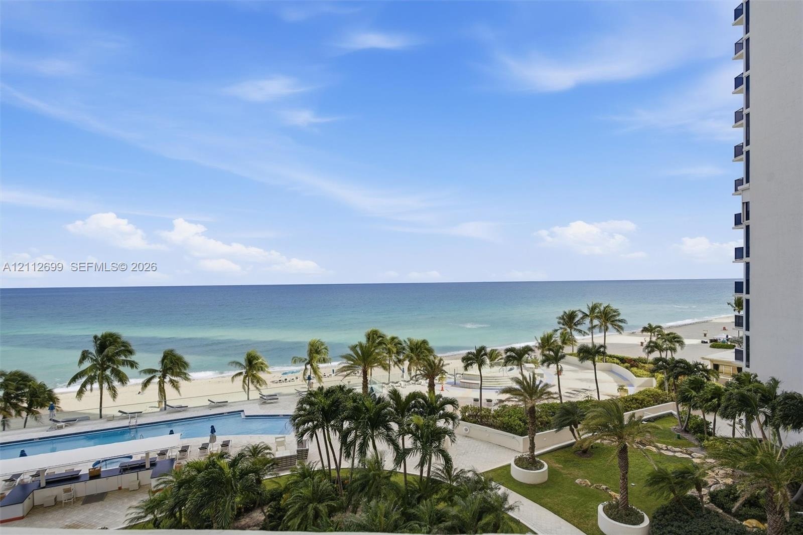 Elevated perspective featuring direct oceanfront access, a sprawling swimming pool with surrounding terrace, landscaped grounds with mature palms, and