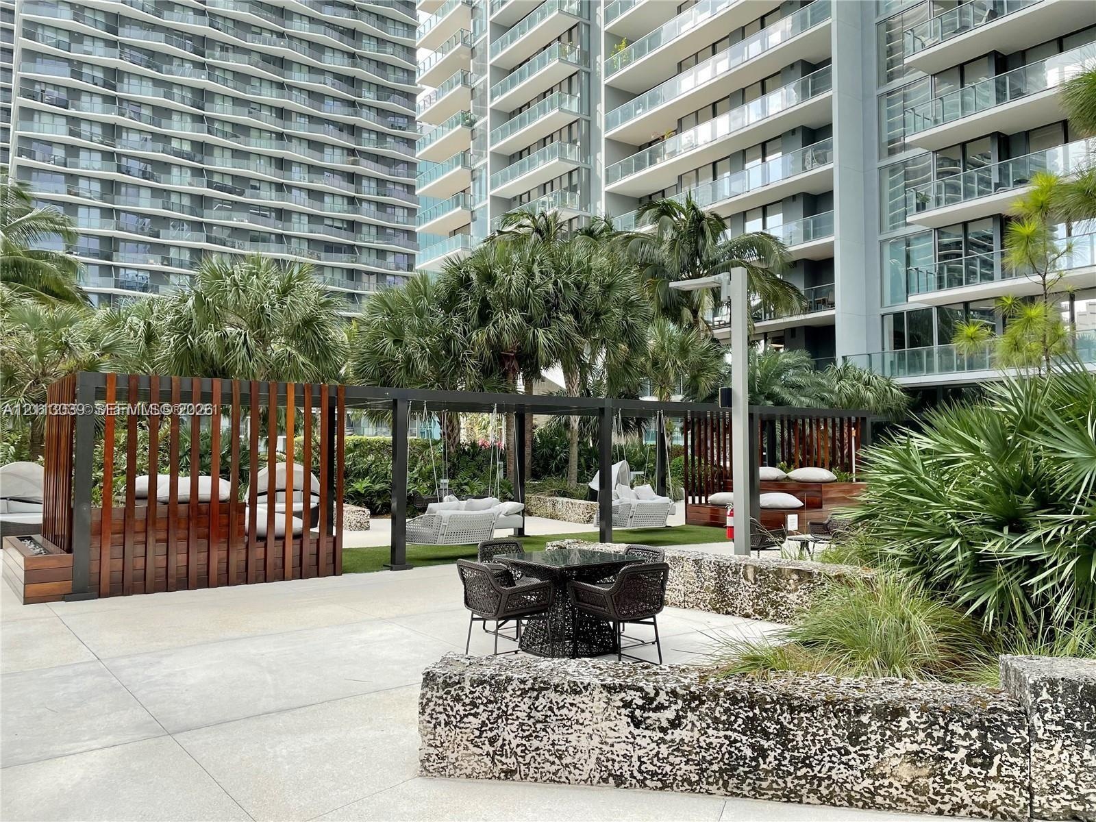 Outdoor terrace featuring large-format concrete pavers, custom dark wood-slatted privacy screens, a natural stone retaining wall, and integrated metal