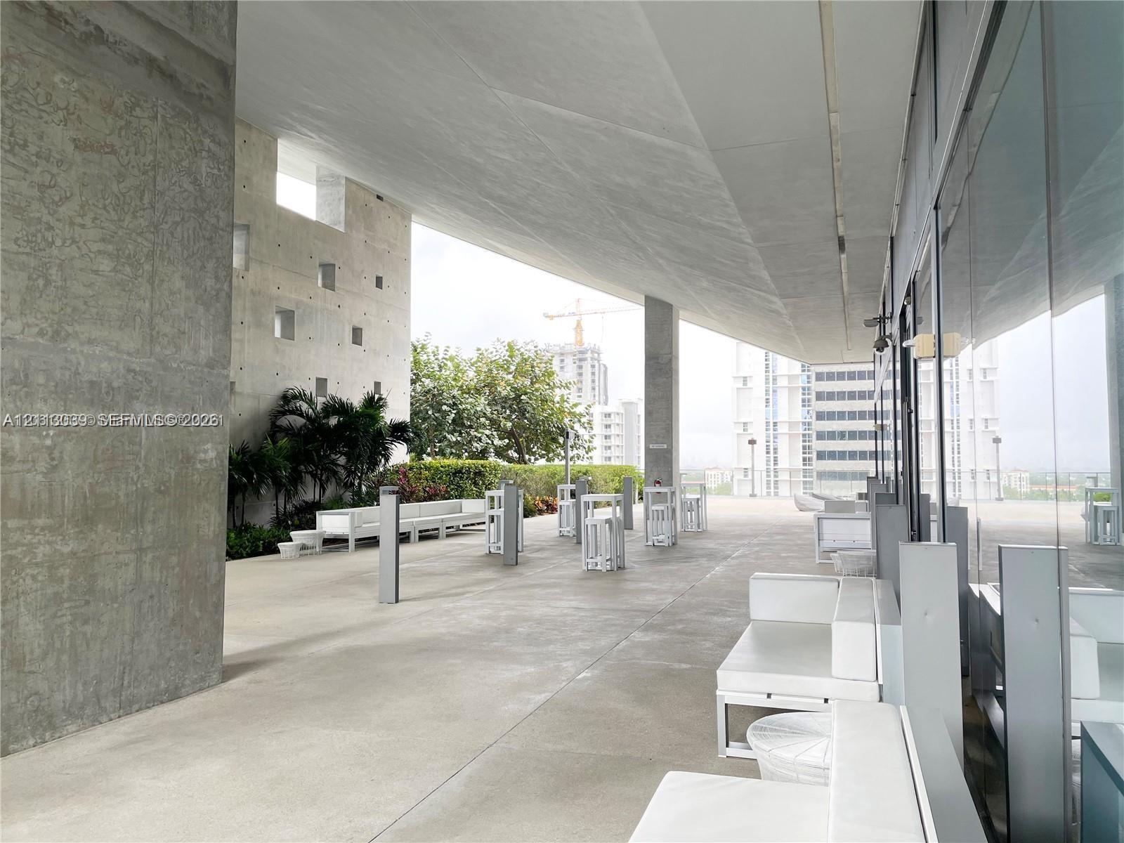 Expansive covered terrace featuring exposed concrete structural elements, floor-to-ceiling glass paneling, and integrated landscape planters
