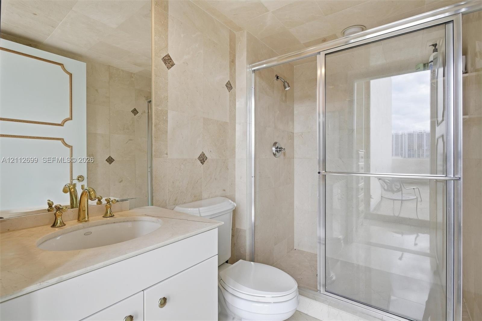 Stone-tiled bathroom featuring a vanity with a drop-in sink, gold-toned hardware, large wall-mounted mirror, and a walk-in shower with glass enclosure