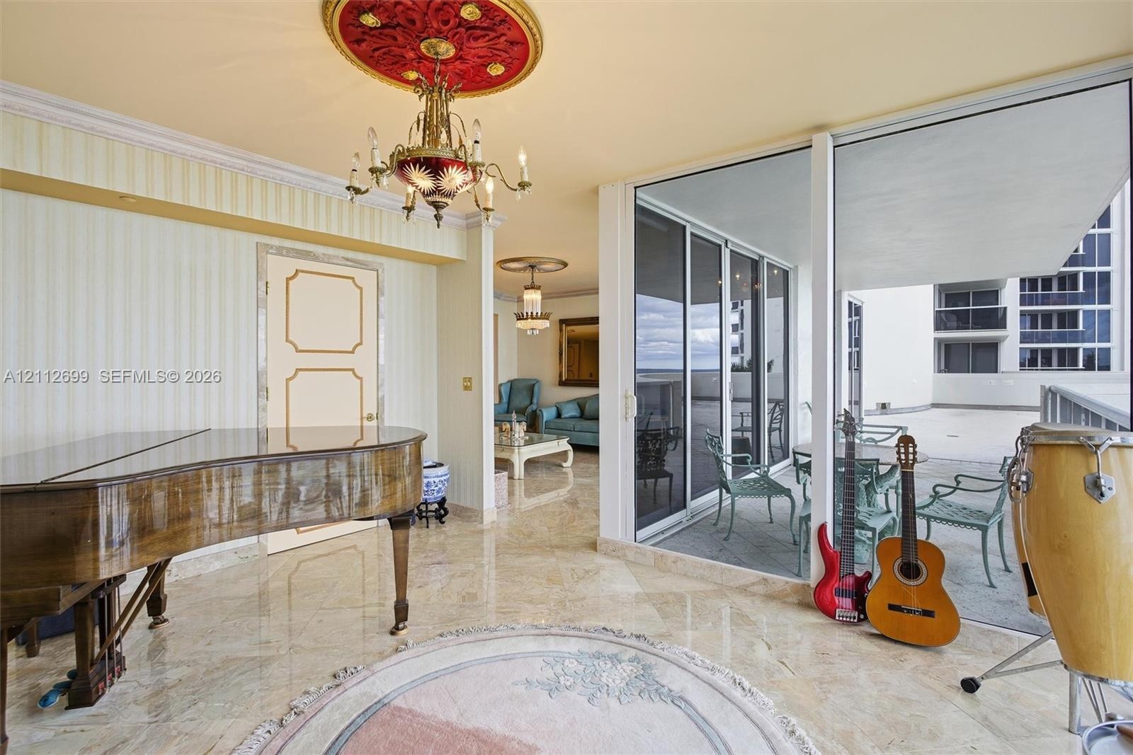 Polished stone flooring, intricate ceiling medallions with ornate light fixtures, and wall-to-wall sliding glass doors opening to an expansive balcony