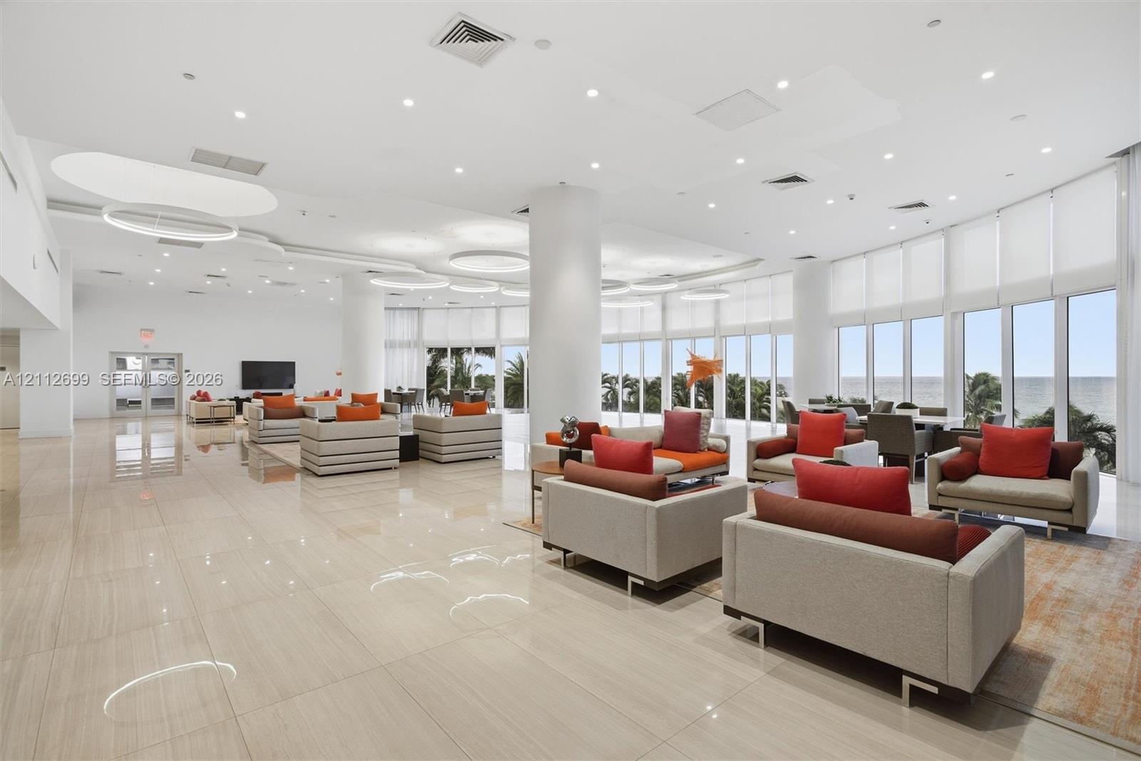 Expansive open-concept space featuring polished tile flooring, floor-to-ceiling windows, recessed lighting, and integrated circular light fixtures
