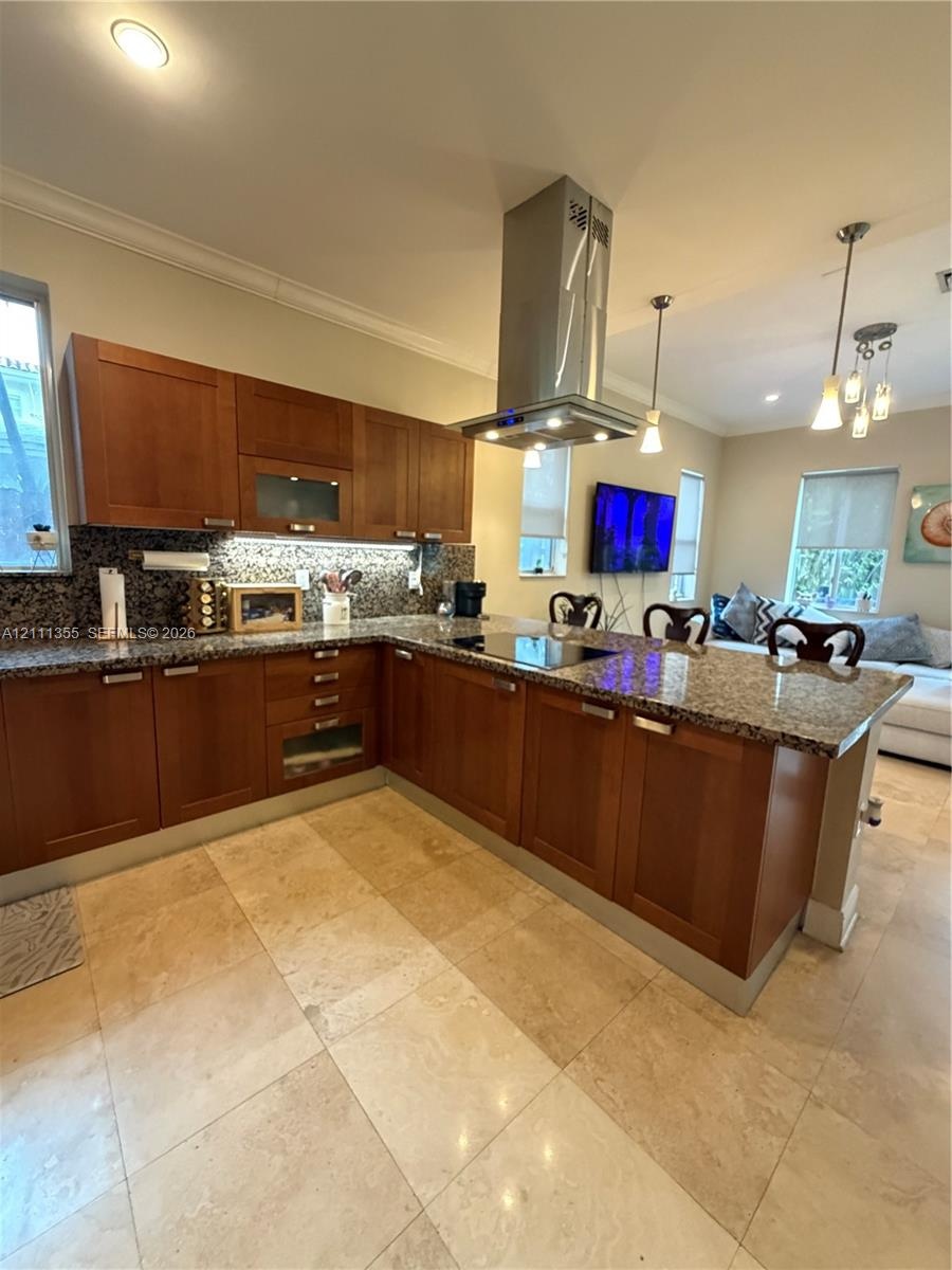 Kitchen featuring shaker-style wood cabinetry, stone countertops, stainless steel chimney-style range hood, integrated cooktop, and neutral stone tile
