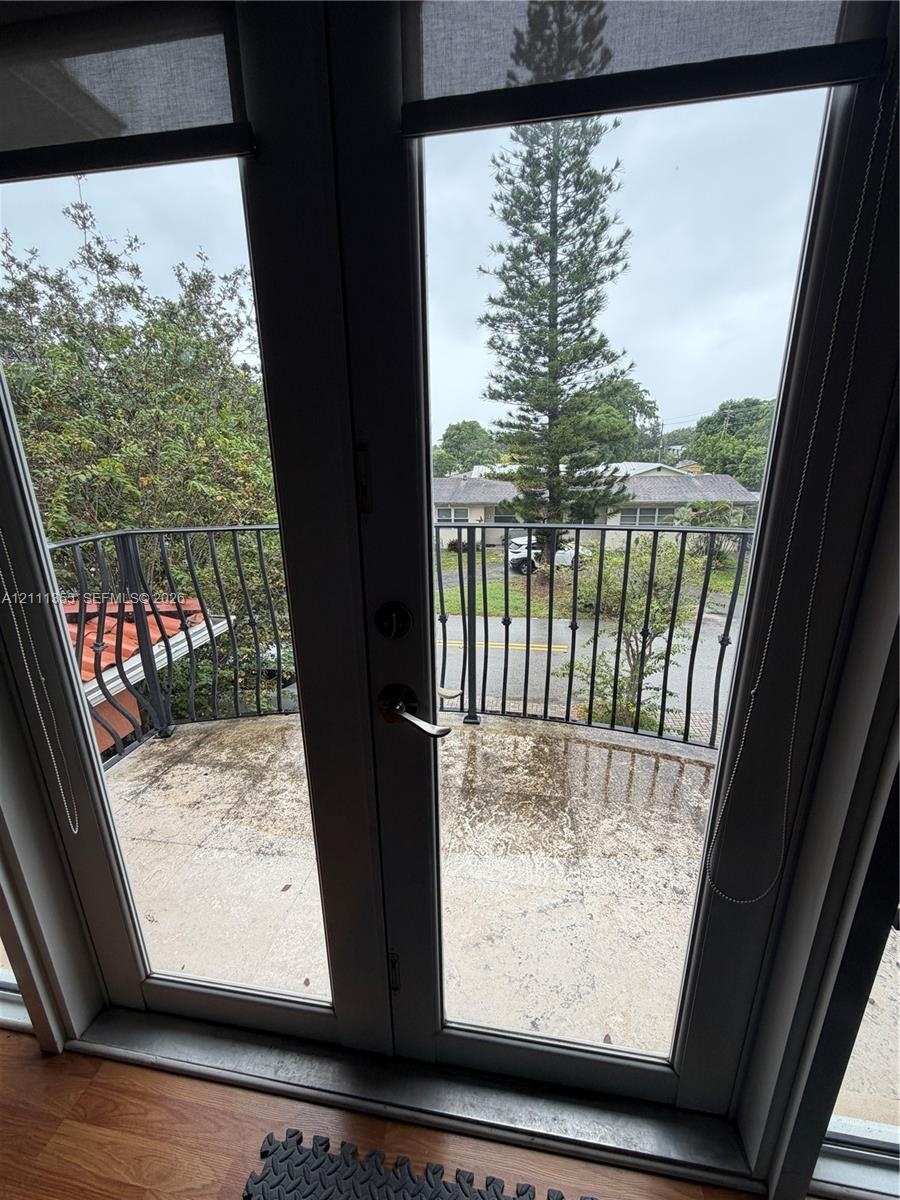 Double glass door entry to a private balcony featuring a wrought iron railing and wood-finish flooring
