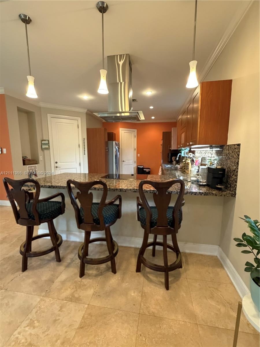 Kitchen featuring an expansive stone countertop, stainless steel ceiling-mounted vent hood, natural stone tile flooring, three pendant lights, and woo