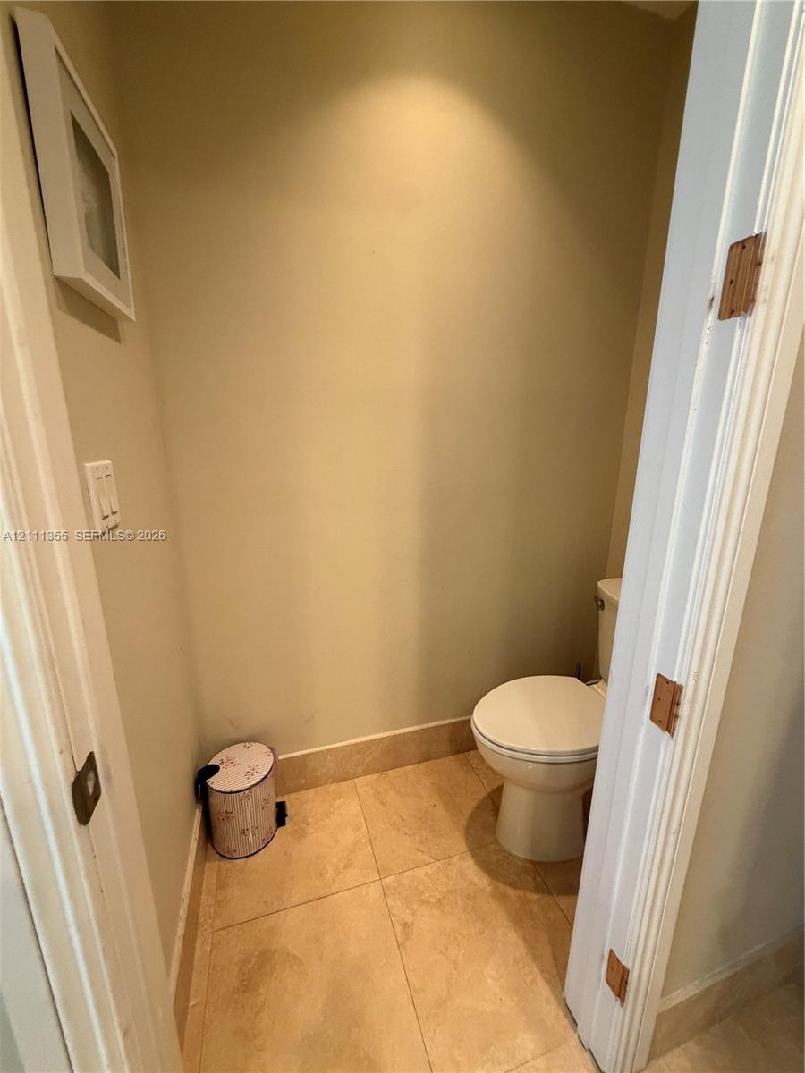 Restroom featuring large-format ceramic floor tiling, neutral wall paint, and a classic white porcelain toilet