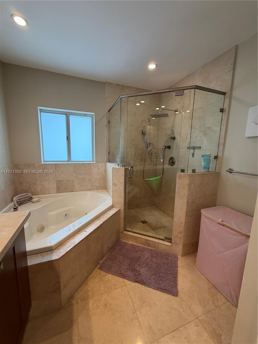 Jetted soaking tub and walk-in shower with a glass enclosure and wall-mounted rainfall showerhead, complemented by neutral-toned stone tile flooring a