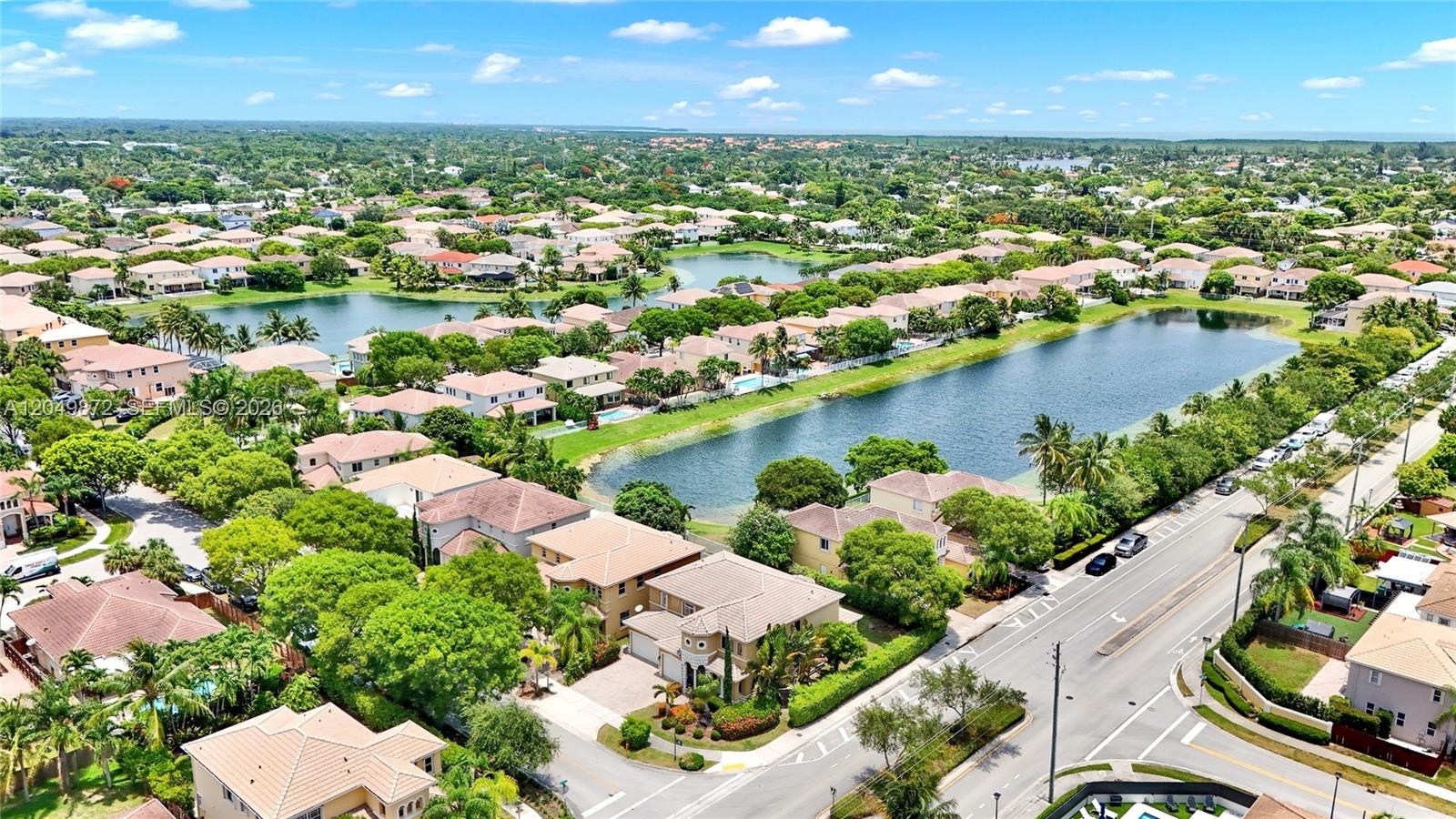 Aerial perspective featuring a multi-story residence with a concrete tile roof, paver driveway, integrated multi-car garage, and lush perimeter landsc