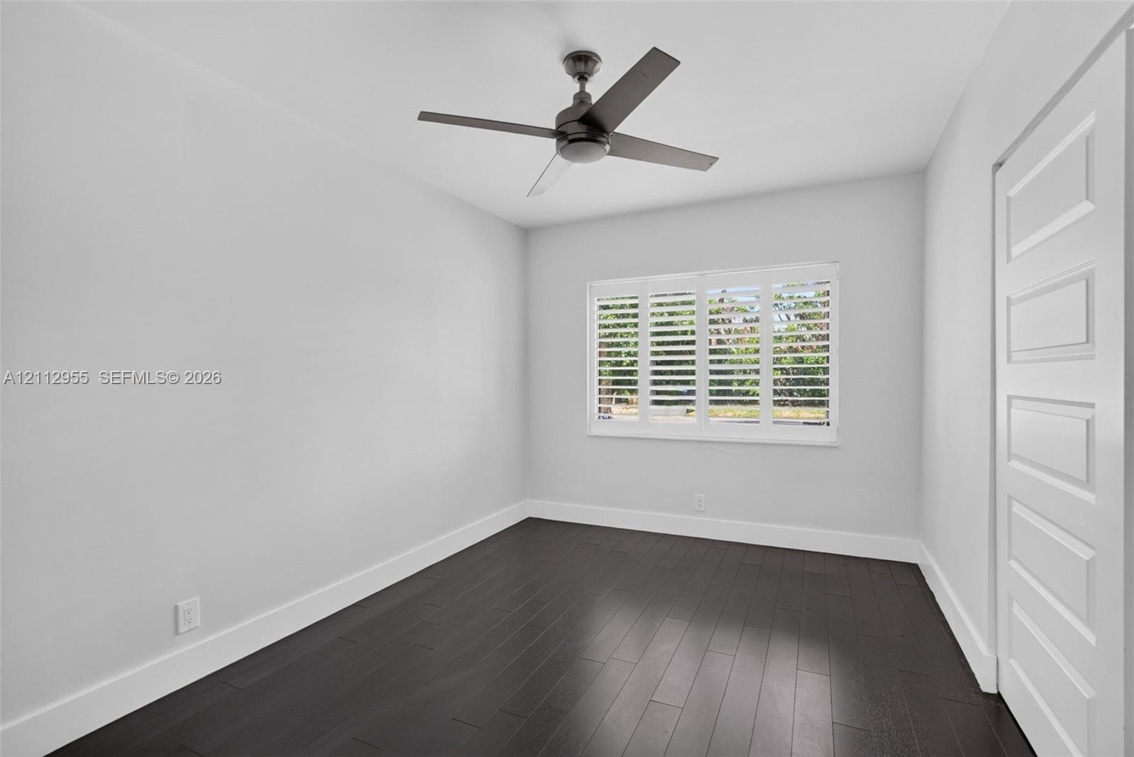 Room featuring wood-finish flooring, plantation shutters, and a four-blade ceiling fan