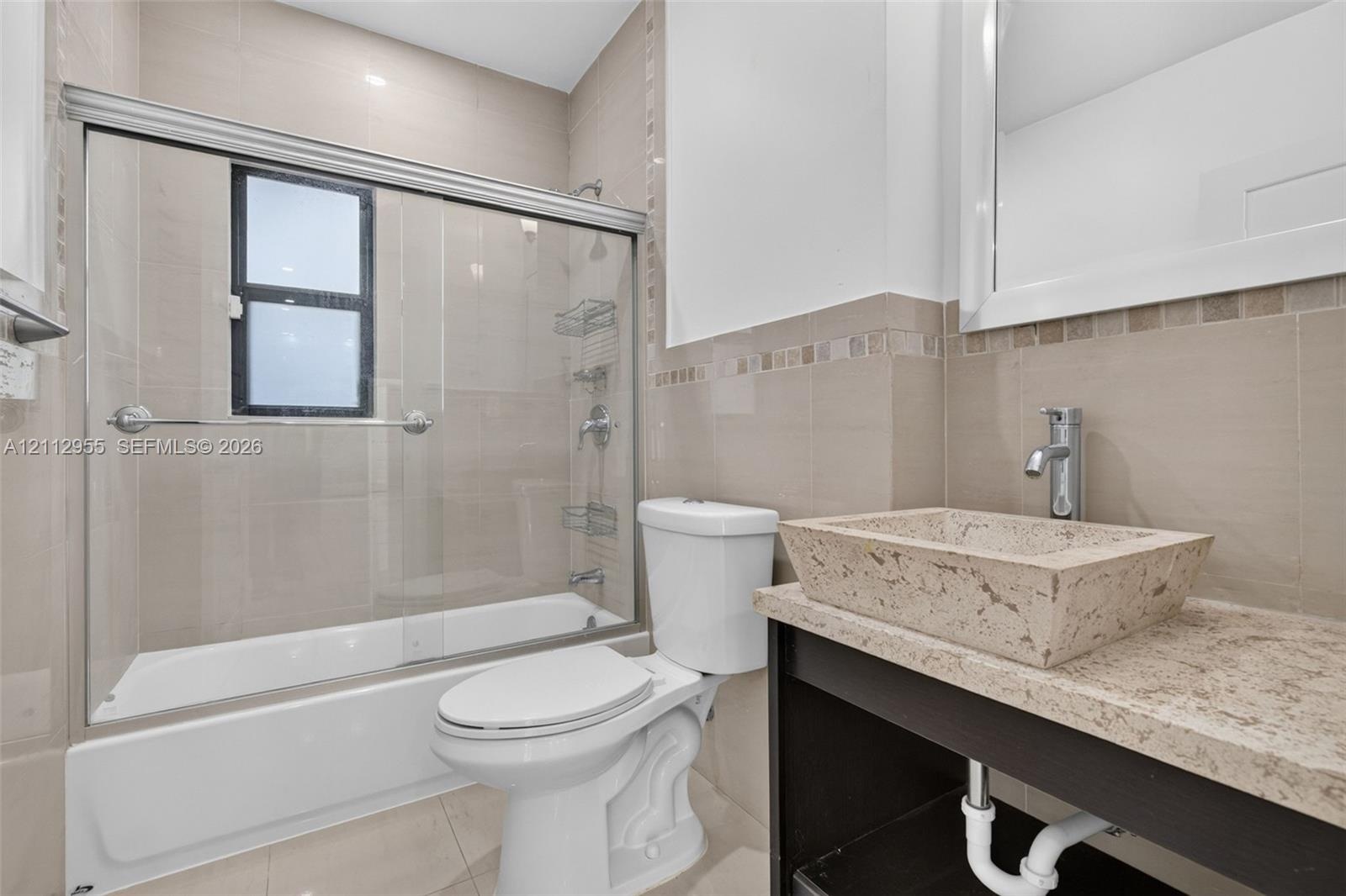 Bathroom featuring a custom stone vessel sink with a chrome faucet, solid-surface vanity countertop, glass-enclosed shower with tiled walls, and decor