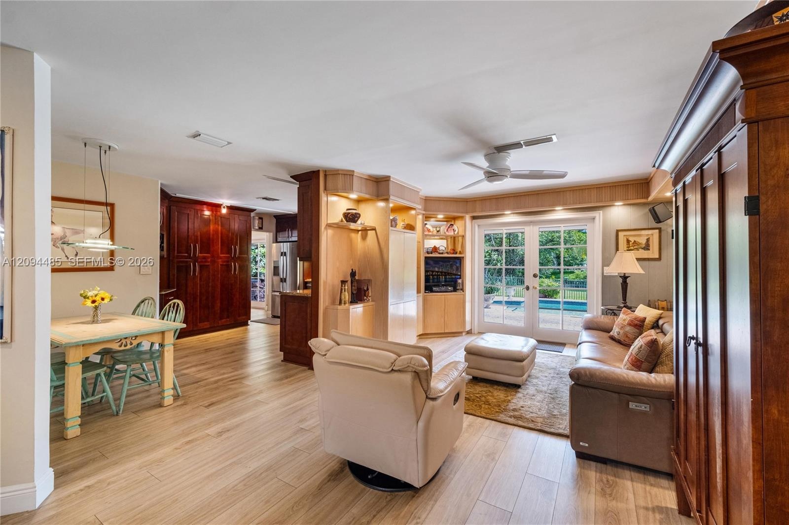 Open-concept interior featuring light wood-finish flooring, custom built-in cabinetry, dual ceiling fans, and glass-paned French doors