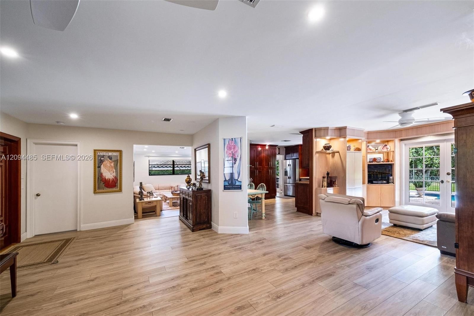 Open-concept interior featuring light wood-finish flooring, recessed lighting, built-in light wood cabinetry, and double glass doors providing exterio