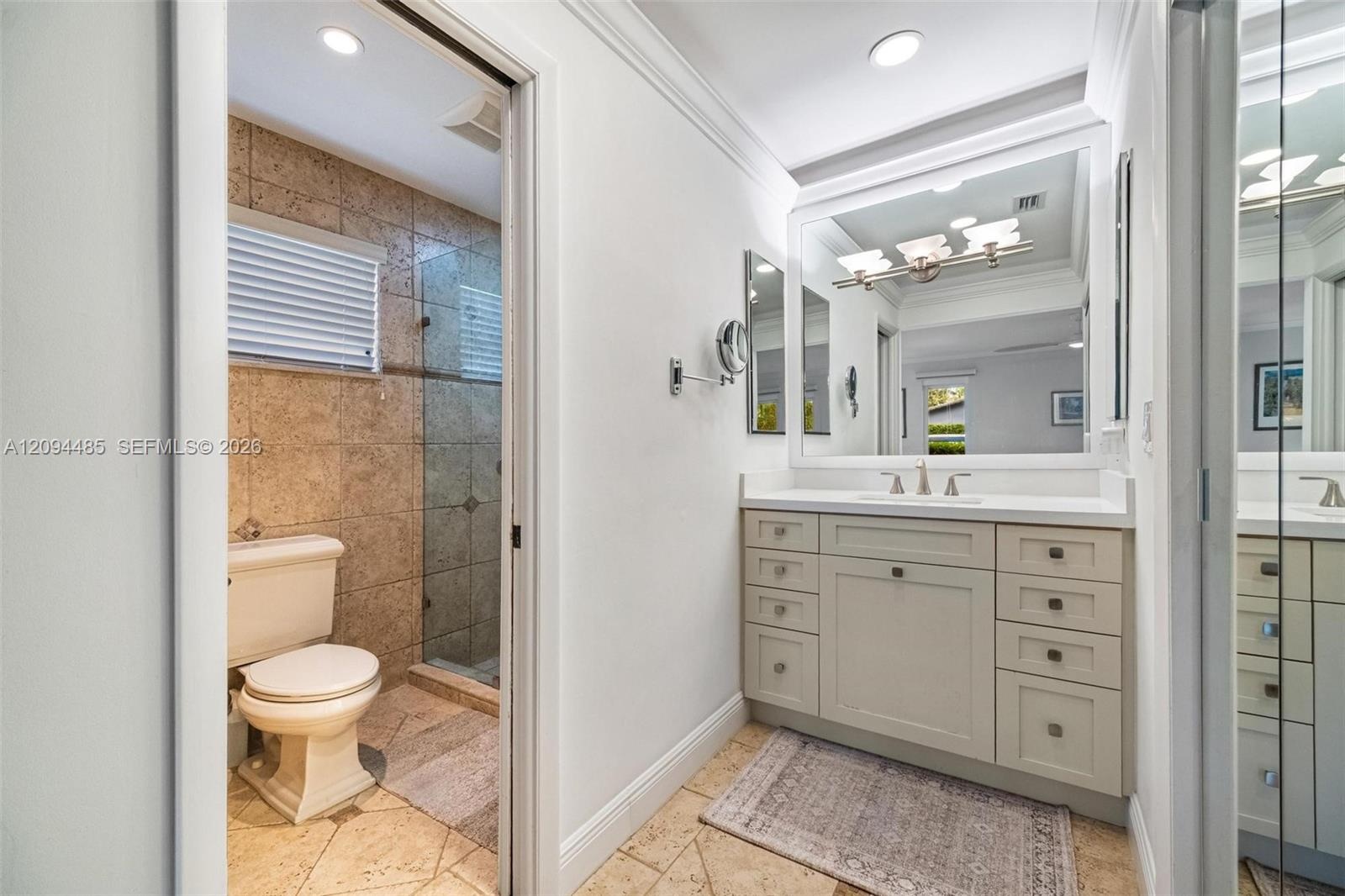 Vanity featuring a white countertop with an integrated basin, shaker-style cabinetry with metallic hardware, large-format wall mirror, and natural sto