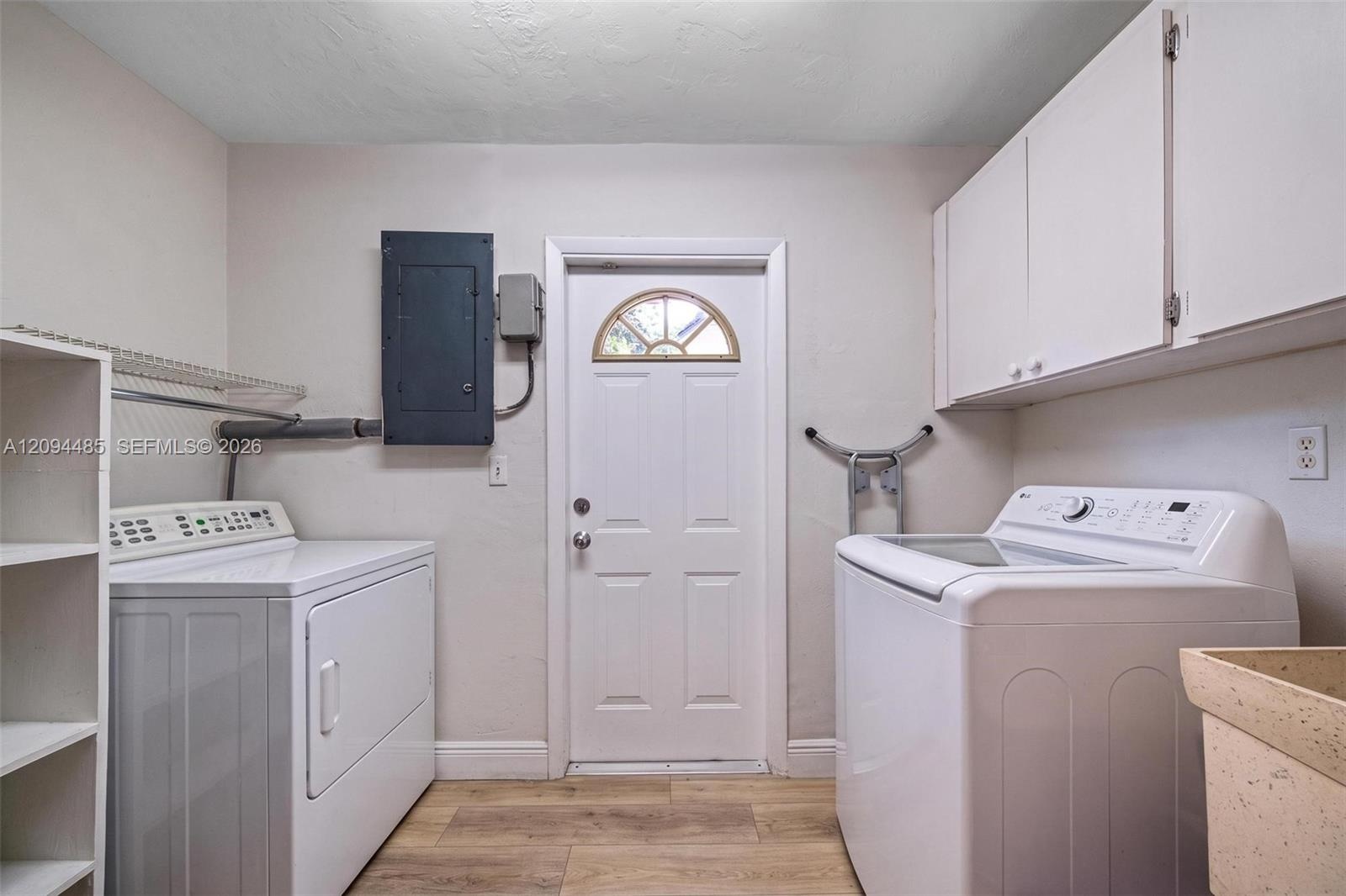 Laundry area featuring wood-finish flooring, white upper wall-mounted cabinetry, integrated shelving, and a utility sink