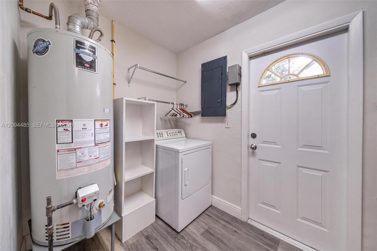 Utility area featuring wood-finish flooring, a white metal exterior door with a semi-circular transom window, and white built-in shelving