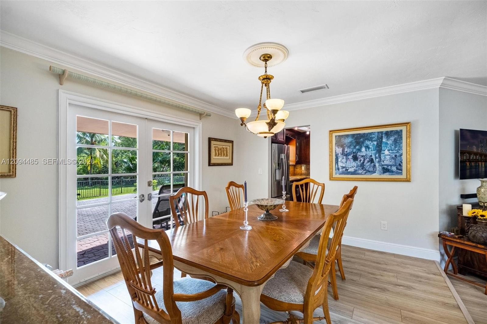 Dining area featuring wood-finish flooring, crown molding, a central multi-light chandelier with a decorative medallion, and double glass-paned doors 
